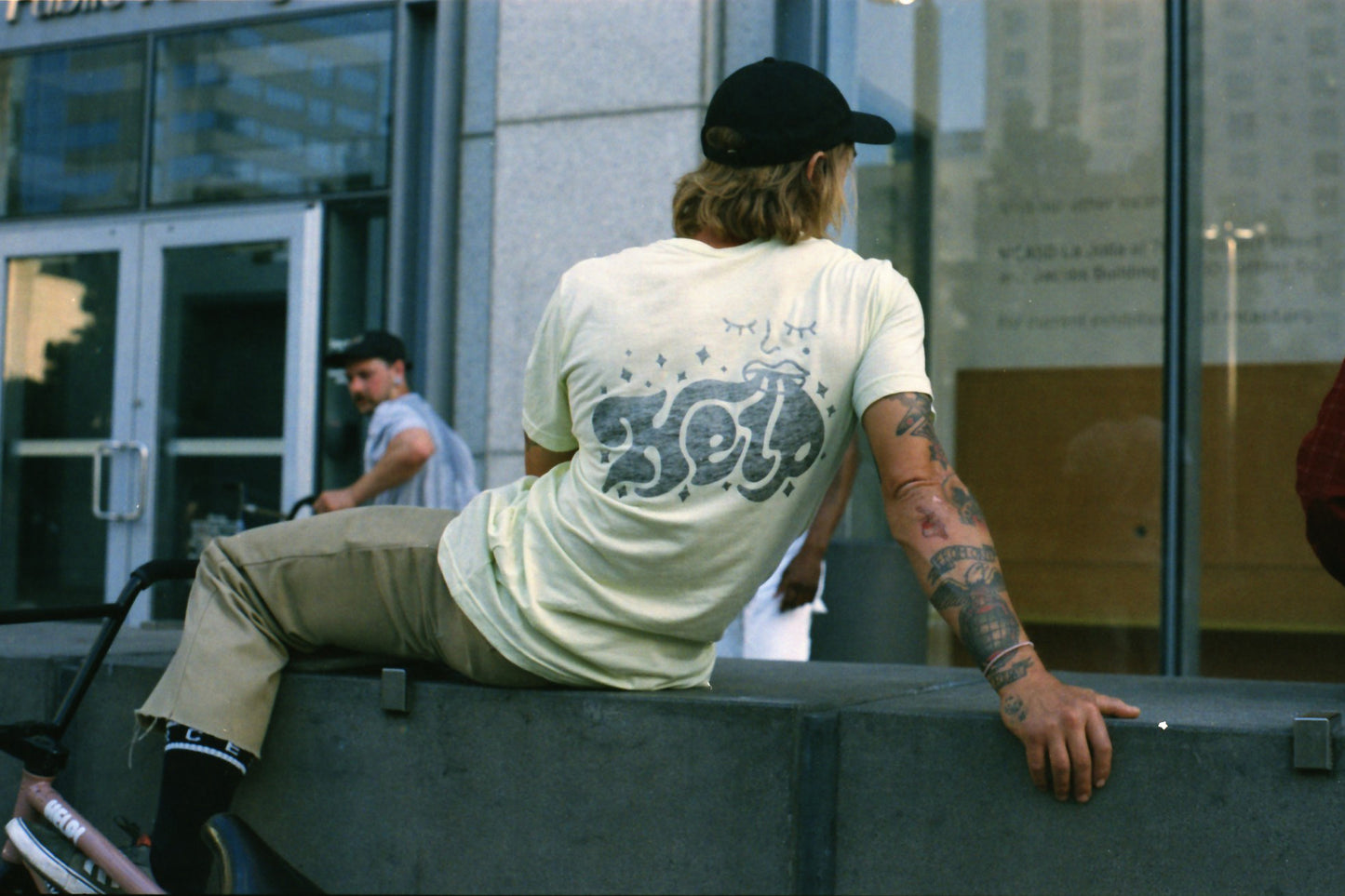 Nathan Williams sitting on a ledge with his back to the camera. he is wearing the "Daily Tee".