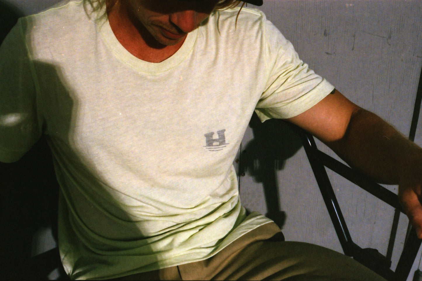 Nathan Williams sitting on his with the front of the "Daily Tee". The shirt is a light pale green and has a small "sinking H" logo on the left chest. 